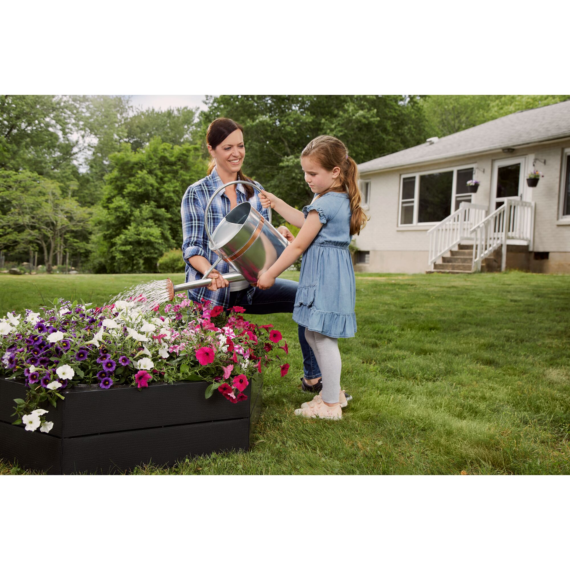 child watering flowers that are planed in a black and decker raised garden bed