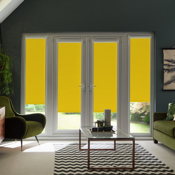 Double glass patio doors covered by bright yellow roller blinds pulled down over lower panes in a modern living room with green armchairs, glass coffee table, chevron rug and plants.