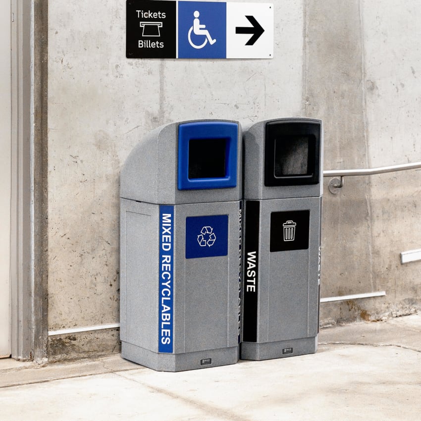 double grey plastic waste and recycling containers with canopy lids and color coded trim openings and body labels in a subway station