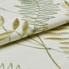 Cream linen fabric with gold and green embroidered fern and leaf motifs, folded to reveal raised satin and outline stitches catching light; close-up studio view with soft, diffuse lighting.
