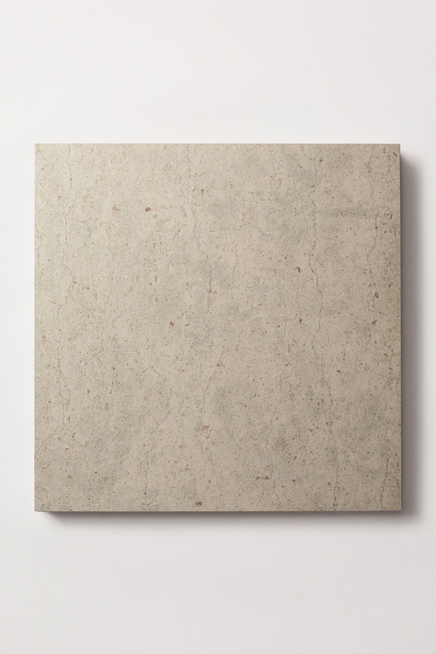 a square limestone tile in medium-grey beige color, marked striations and flecks of white.