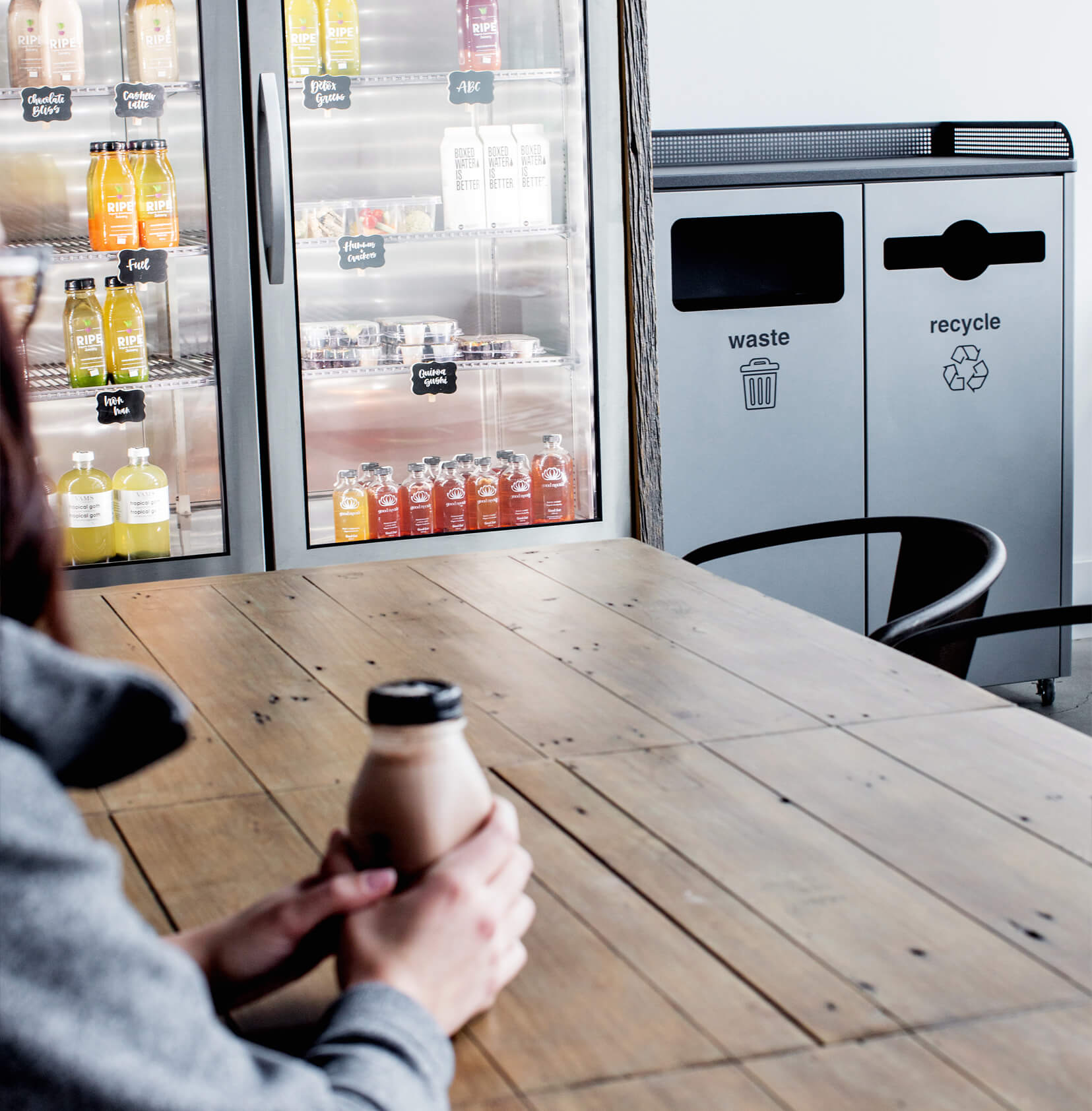 durable metal recyclables and trash bin in a coffee shop showing a woman sitting at a table with a drink