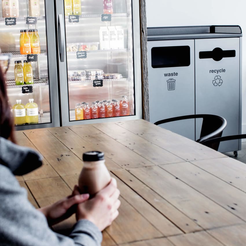 durable metal recyclables and trash bin in a coffee shop showing a woman sitting at a table with a drink