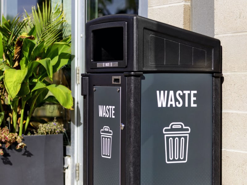 black recycled plastic waste container with sloped canopy lid and large body signs for improved waste diversion