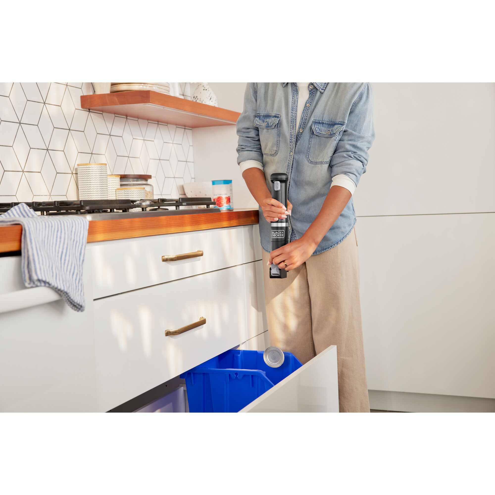 Talent lifting the lever on the black, BLACK+DECKER kitchen wand can opener to discharge the can lid in to the recycling bin