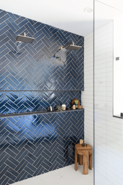a blue herringbone tiled shower with a wooden bench.