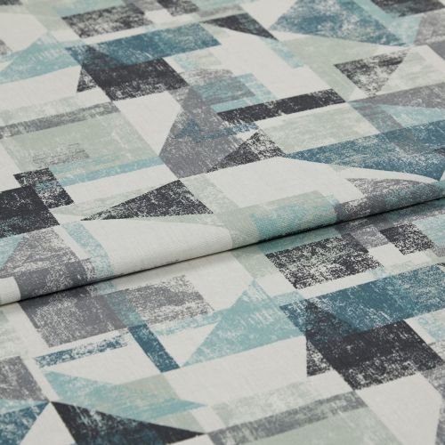 Upholstery fabric (distressed geometric teal, grey, black triangles and squares) folded with overlapping crease; close-up on a flat surface in neutral studio lighting, no visible surroundings.