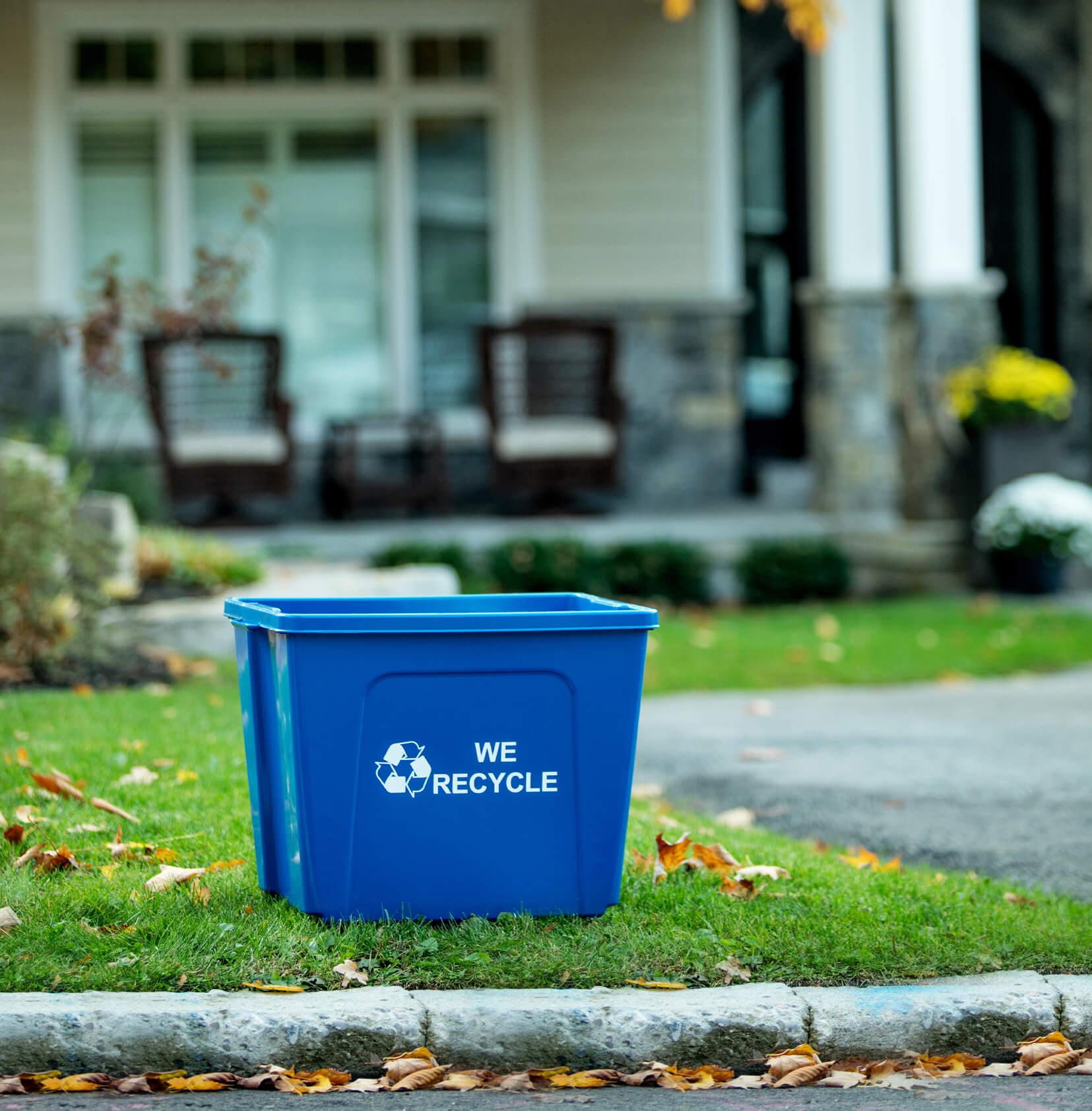 large blue recycling bin with we recycle on the side placed at the curb of an upscale home