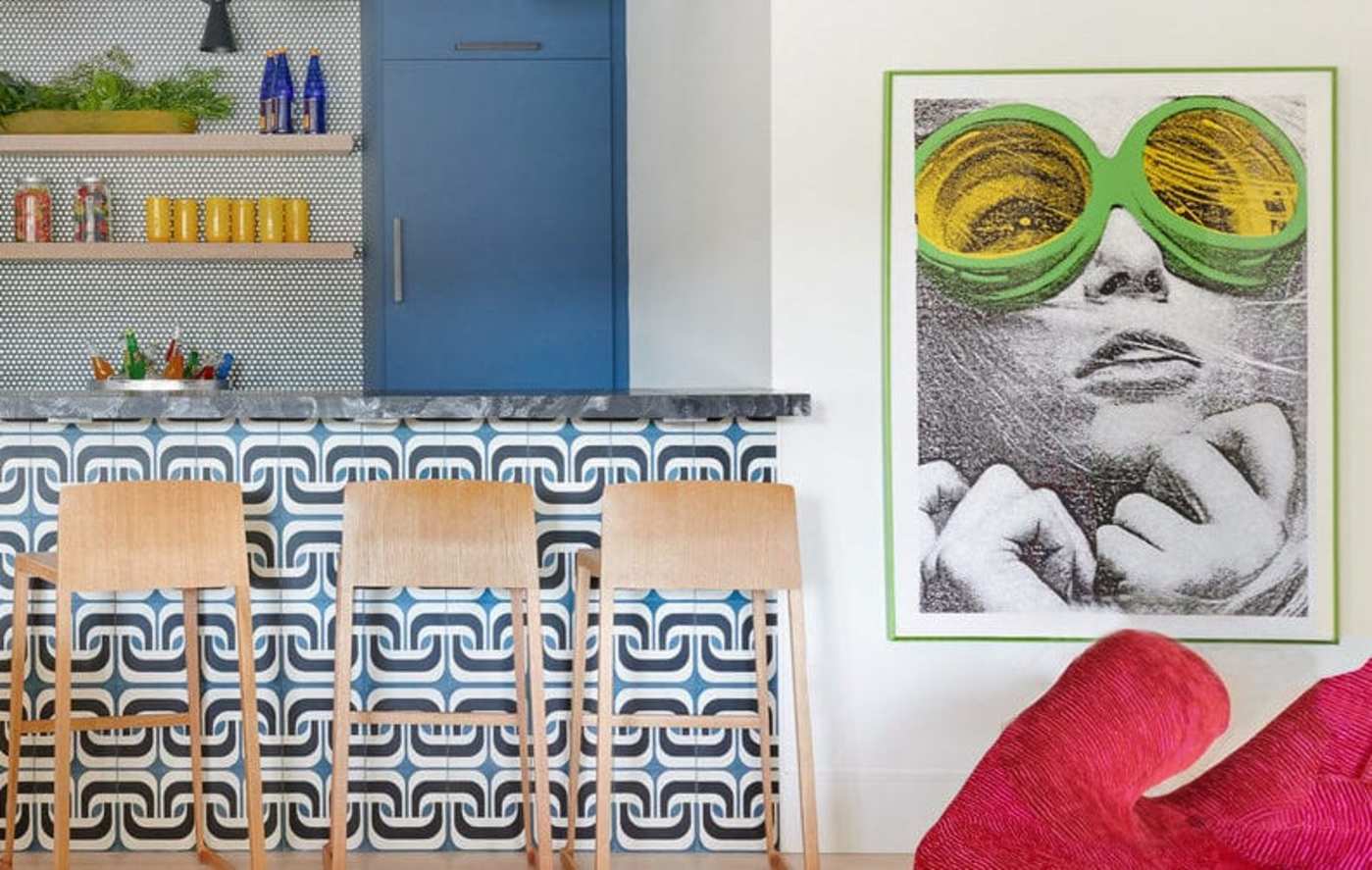 a kitchen with a tuked counter, colorful chairs and a painting on the wall.