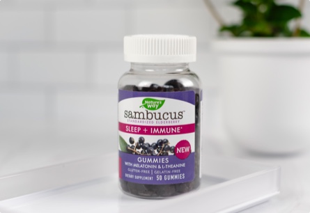 A bottle of Sambucus Sleep plus Immune gummies sitting on a white tray in front of a white potted plant.