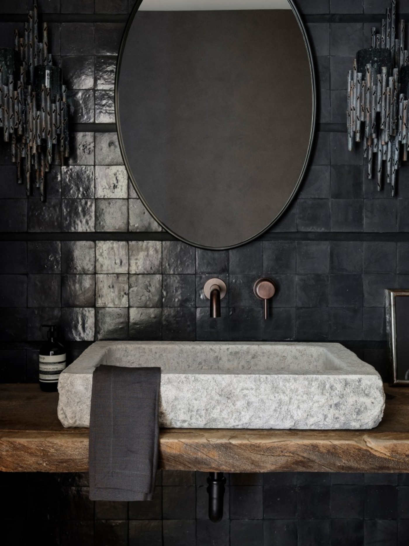 a black tiled backsplash with a stone sink and a mirror.