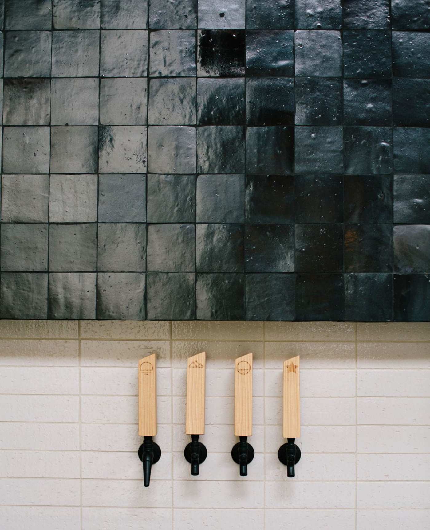 a black tiled wall with a row of wooden taps.