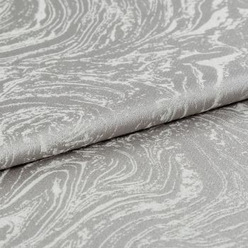 Silver-gray textured jacquard fabric with marbled swirl pattern, folded in overlapping layers; draped and creased; photographed close-up under soft studio lighting with a neutral background.