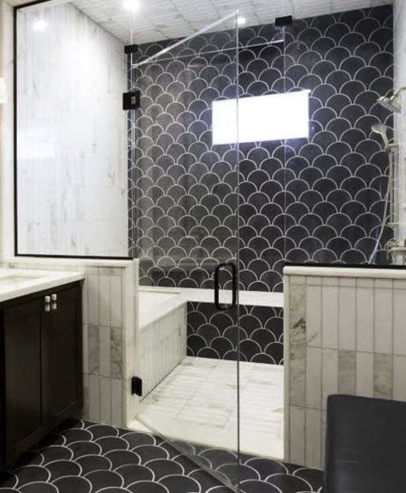 a shower with a black tile wall and a glass door.