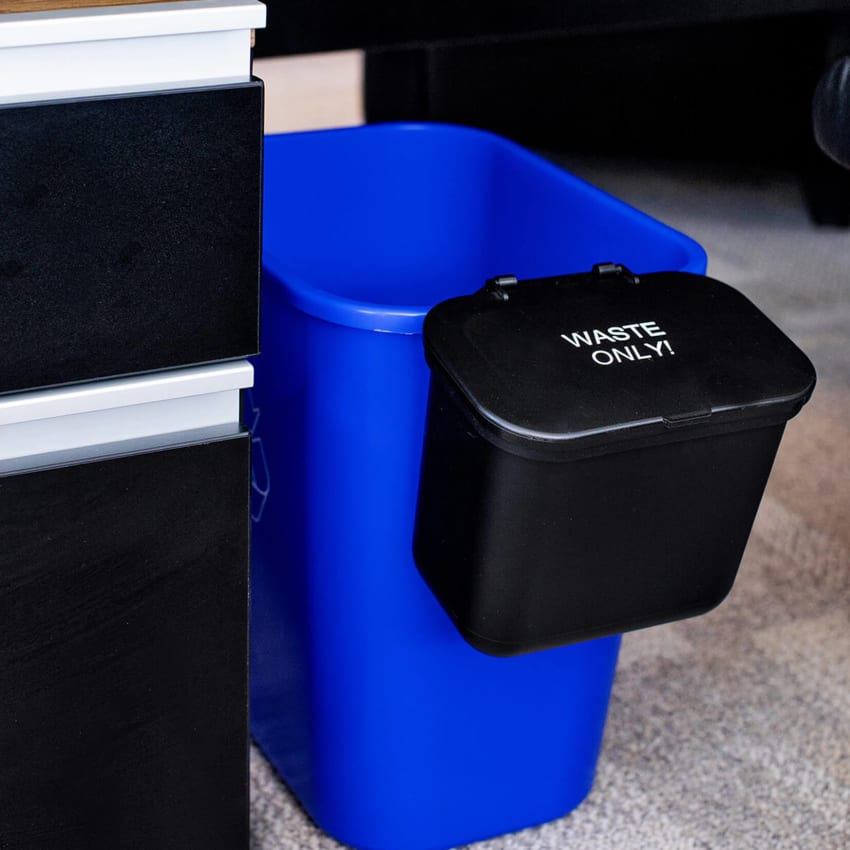 small blue plastic recycling bin with a small black plastic hanging waste container on the side sitting under a desk in an office