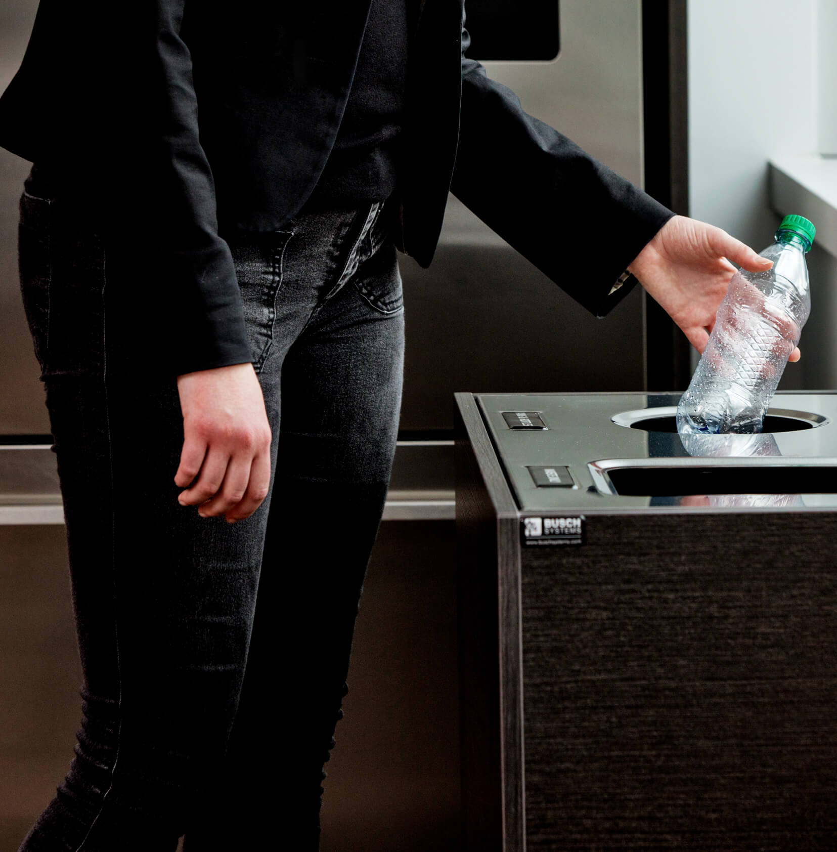 woman dropping a plastic water bottle into a high-end recycling container in an office kitchen