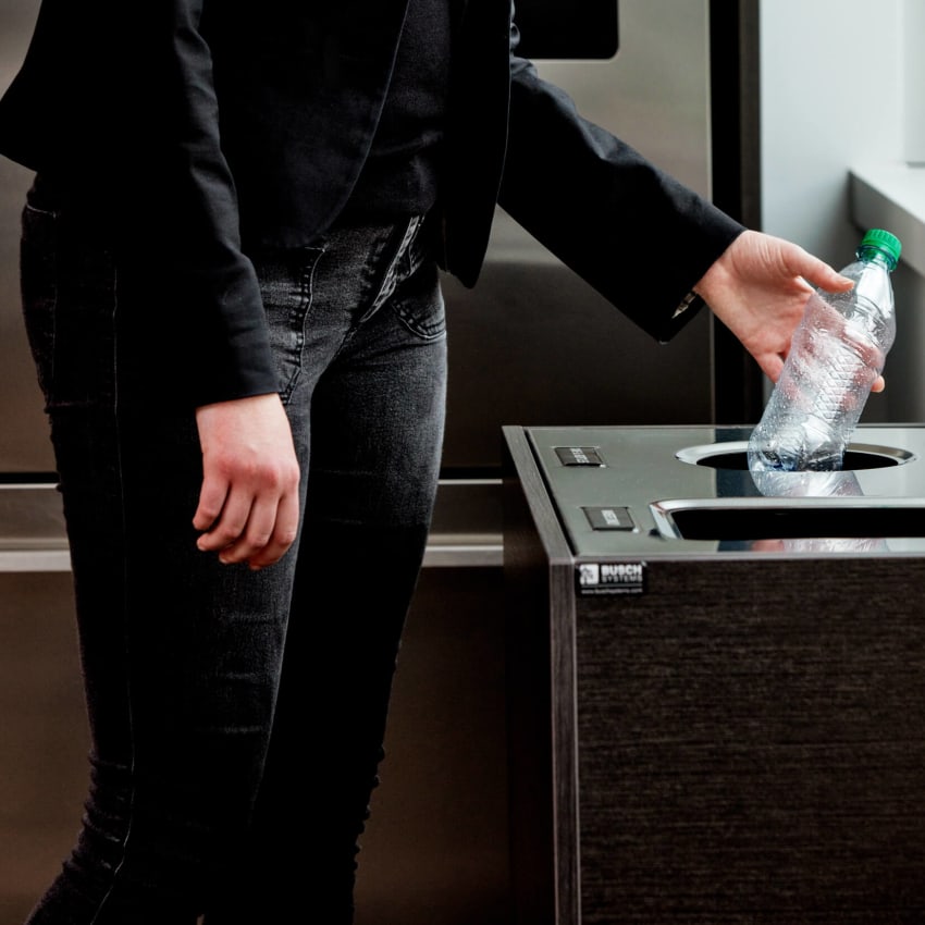 woman dropping a plastic water bottle into a high-end recycling container in an office kitchen