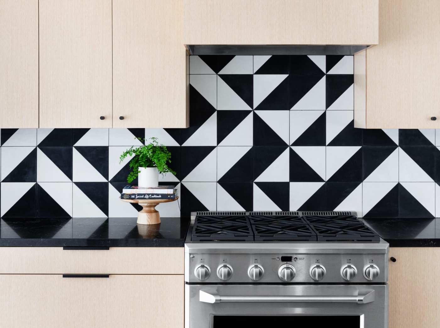 a kitchen with a stove backsplash of black and white geometric tiles.