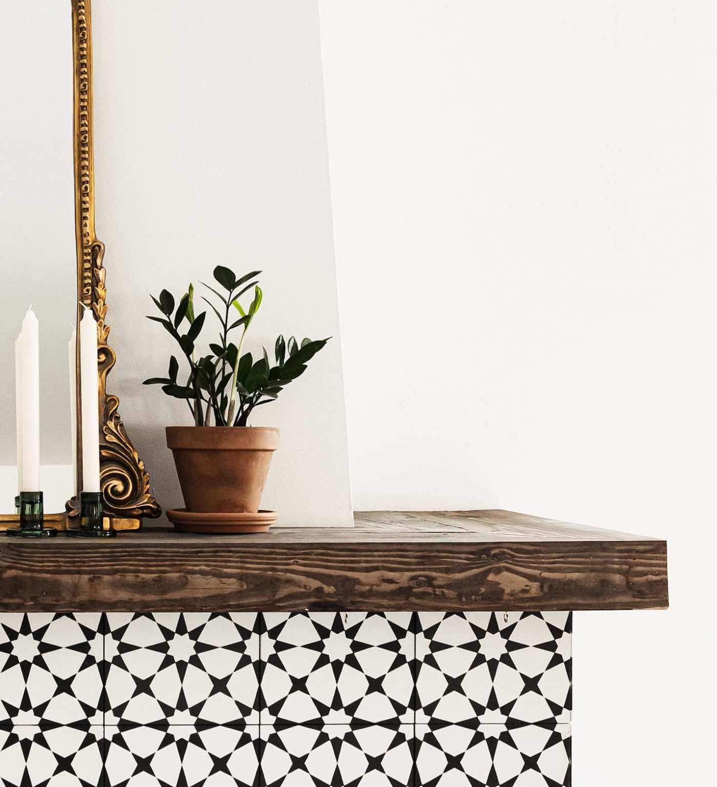 a black and white tiled mantel with a candle and a potted plant.