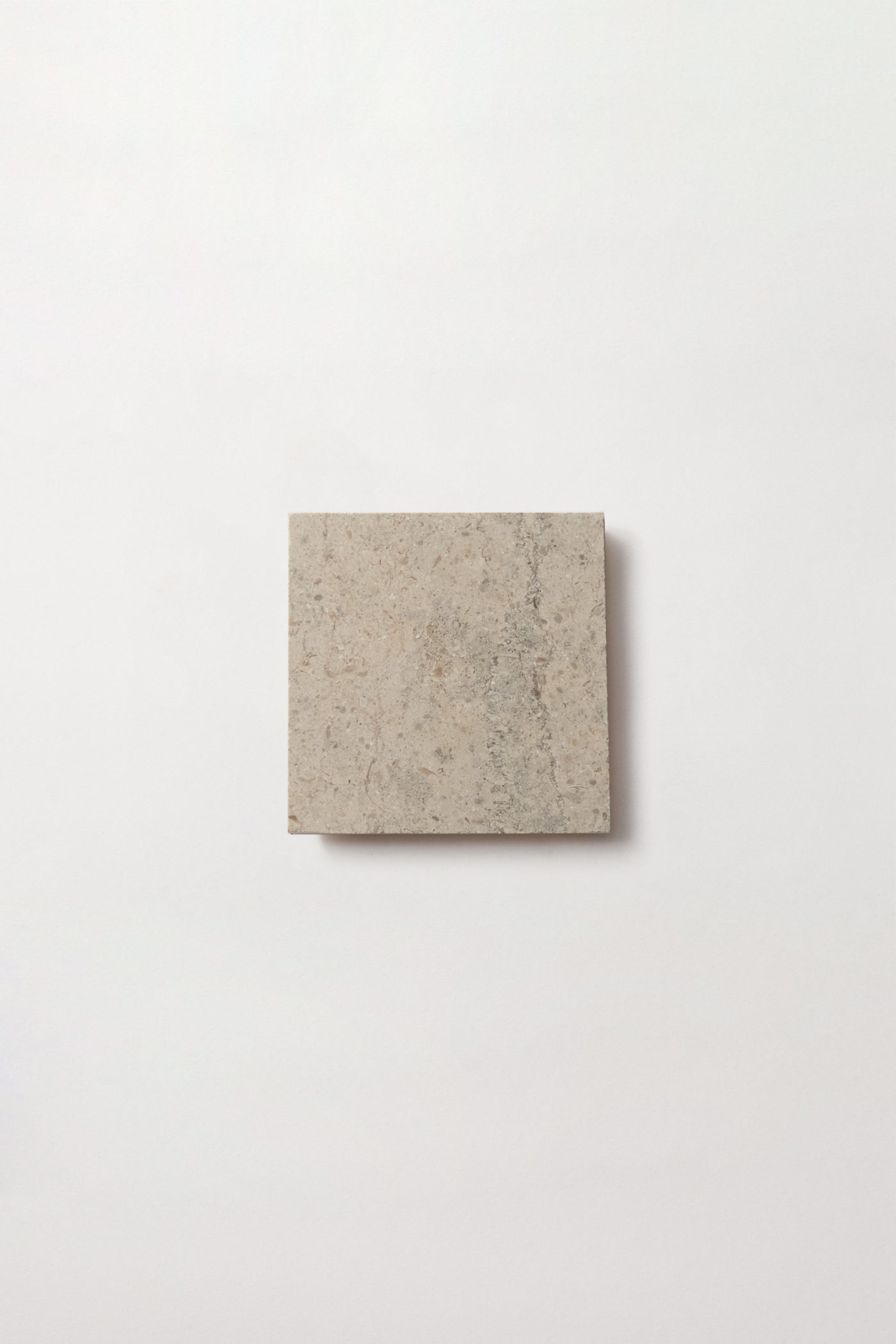 a square limestone tile in medium-grey beige color, marked striations and flecks of white.