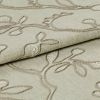 Beige embroidered fabric folded into overlapping layers, showing raised stitched vine-and-leaf motifs in tonal thread; close-up view with soft, even lighting emphasizing texture.