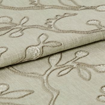 Beige embroidered fabric folded into overlapping layers, showing raised stitched vine-and-leaf motifs in tonal thread; close-up view with soft, even lighting emphasizing texture.