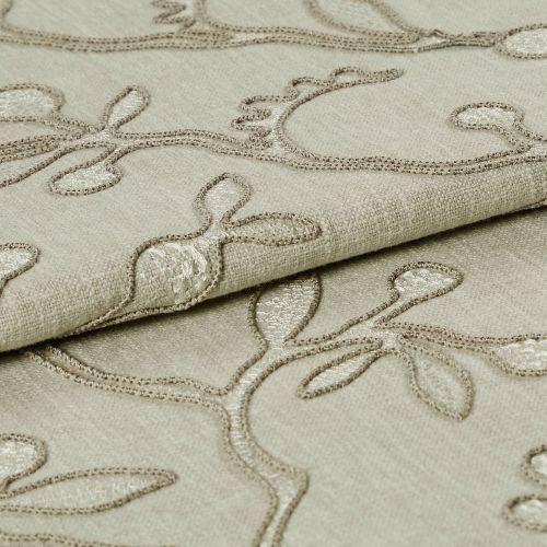 Beige embroidered fabric folded into overlapping layers, showing raised stitched vine-and-leaf motifs in tonal thread; close-up view with soft, even lighting emphasizing texture.