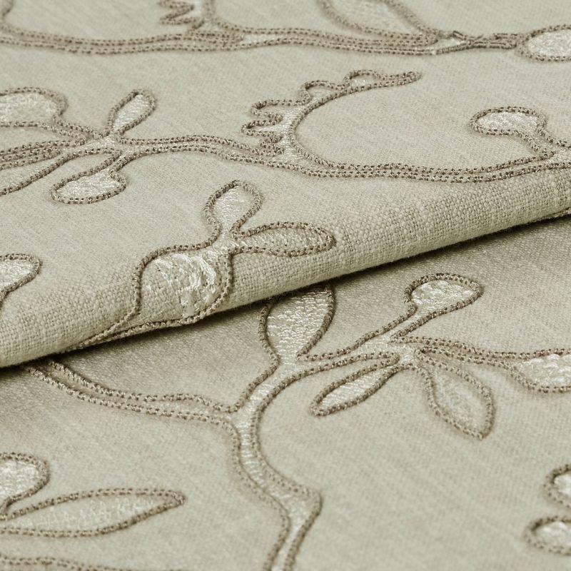 Beige embroidered fabric folded into overlapping layers, showing raised stitched vine-and-leaf motifs in tonal thread; close-up view with soft, even lighting emphasizing texture.