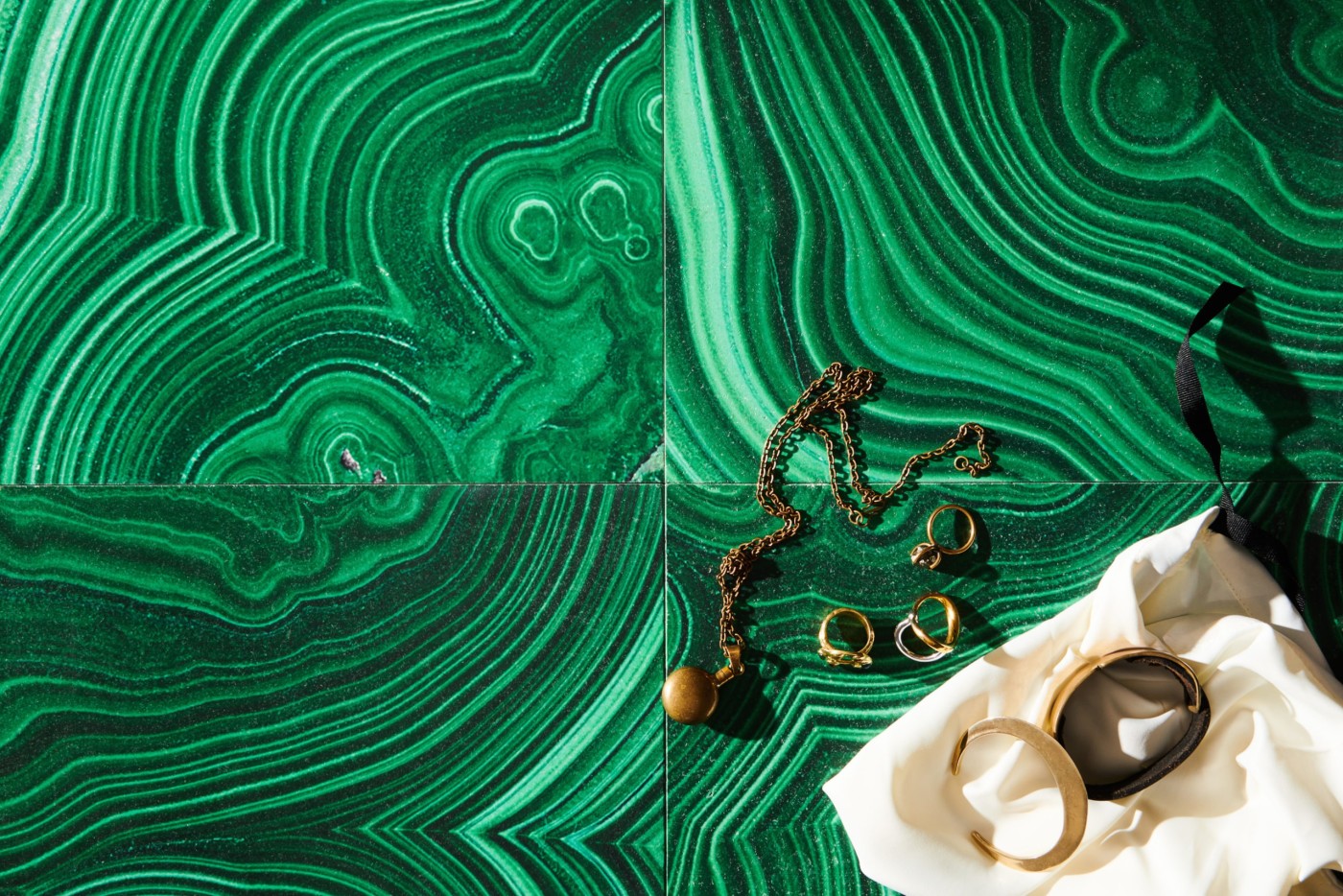 a white bag and some gold jewerly on an emerald green tiled surface.