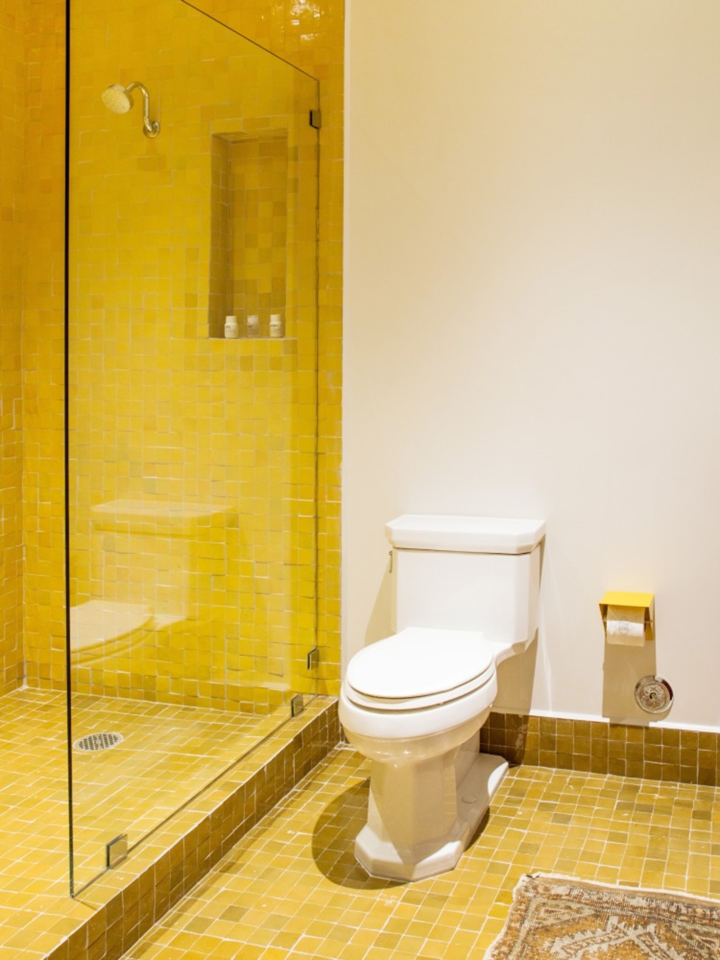 a yellow tiled bathroom with a toilet and shower.