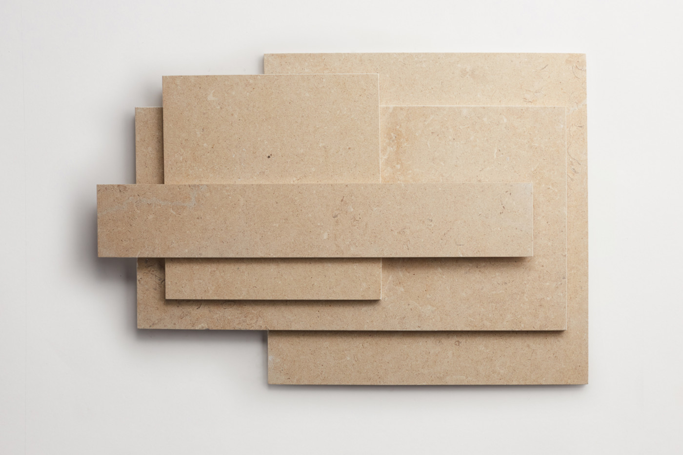 Tan limestone tiles of various shapes stacked on a white background.