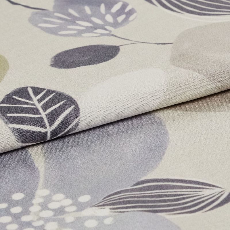 A folded beige curtain fabric with stylized gray and lavender leaf prints (textured knit), overlapping to show the hem and pile, photographed close-up on a neutral surface under soft lighting.