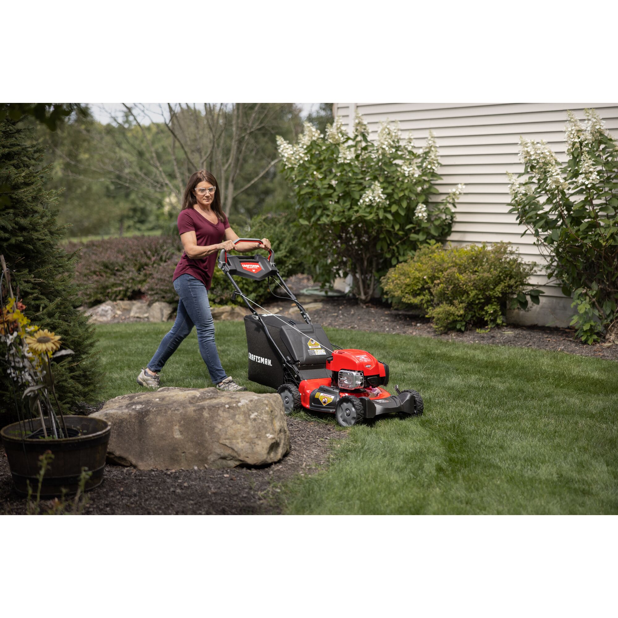 CRAFTSMAN M310 Gas Push Mower mowing around flower bed with large rock