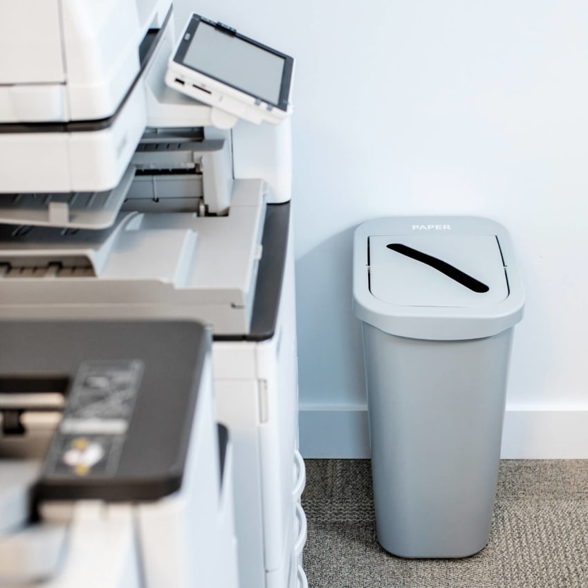 grey plastic paper recycling container sitting in a business beside the printer for collecting used paper