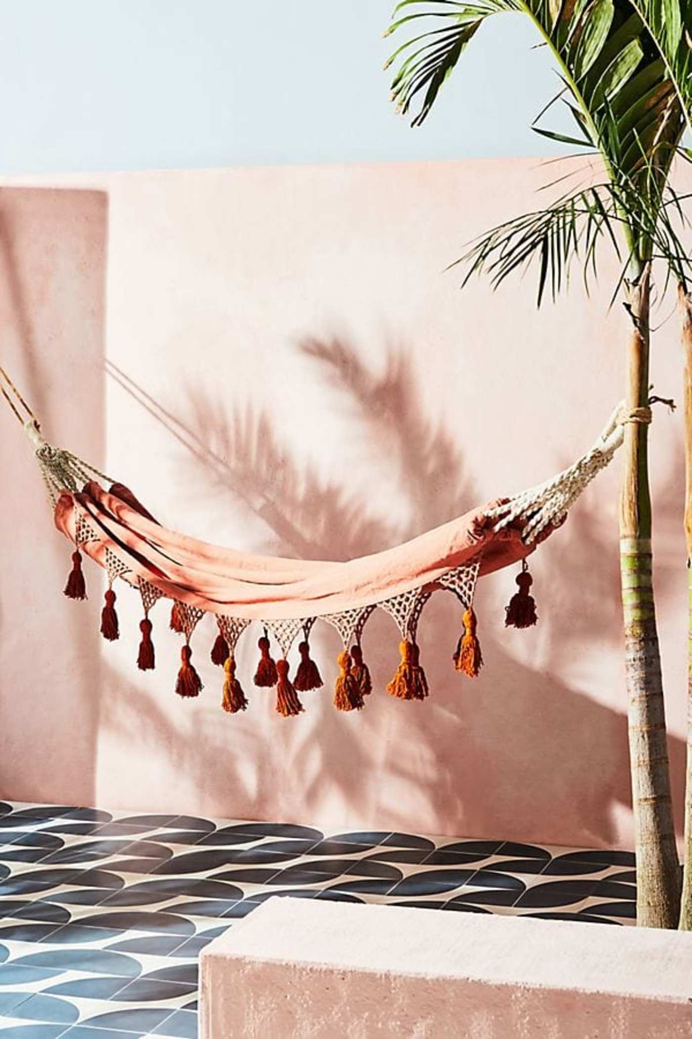 a hammock with tassels hanging from it over a blue and white tiled floor.