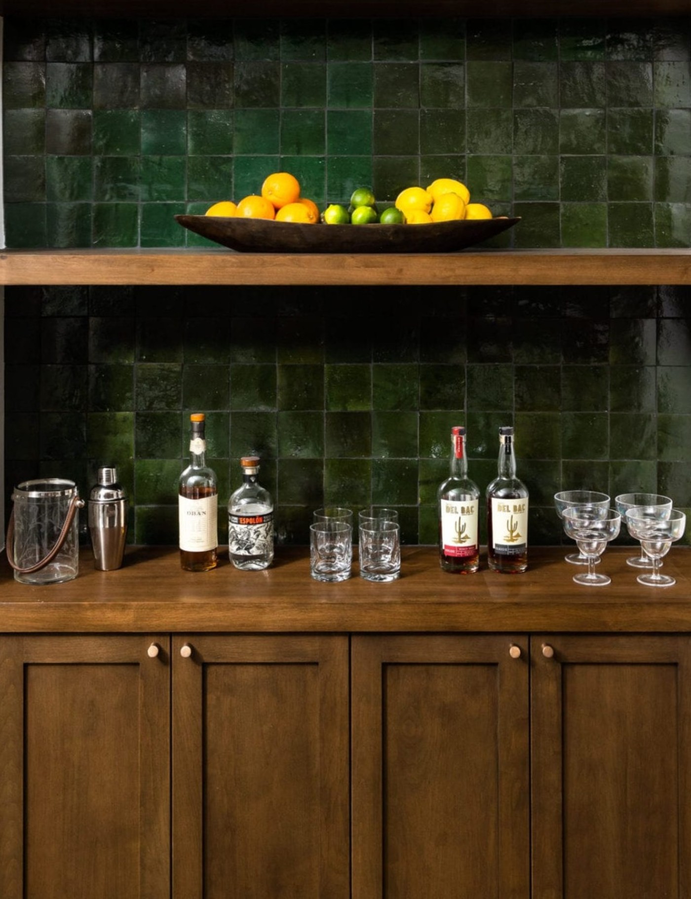 a green tiled bar with bottles and glasses.