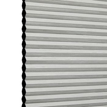 Honeycomb (cellular) blind panel at left edge, white-gray pleated horizontal cells with black hexagonal cell ends; lowered and closed, filtering diffuse light; studio-lit close-up against plain white background.