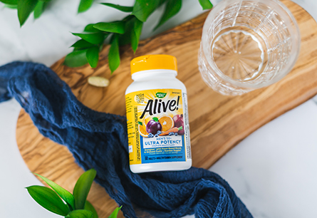 A bottle of Alive! Multivitamins Men's 50+ Ultra tablets on wood cutting board with napkin and glass of water.