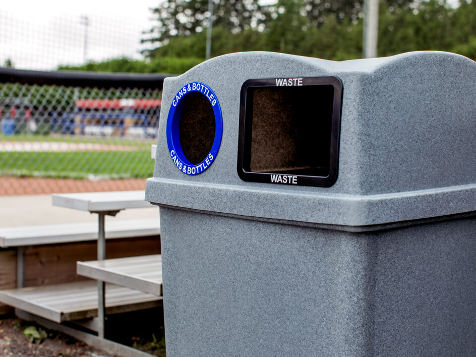 closeup of a waste and recycling bin lid openings made from durable LDPE plastic sitting outdoors at a baseball field beside the bleachers