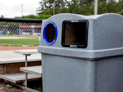 closeup of a waste and recycling bin lid openings made from durable LDPE plastic sitting outdoors at a baseball field beside the bleachers