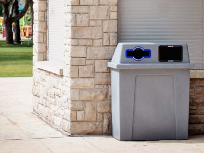 double stream waste and mixed recycling collection container with a sloped lid and durable plastic body outdoors at a community park