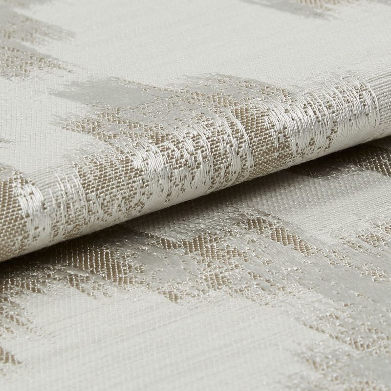 Woven curtain fabric, folded to reveal a metallic-thread abstract pattern and textured weave, reflecting light; close-up, neutral studio lighting.