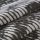 Folded woven fabric with irregular white brushstroke stripes on a dark background — stacked in overlapping layers — close-up of textured, soft textile under neutral, diffuse lighting.