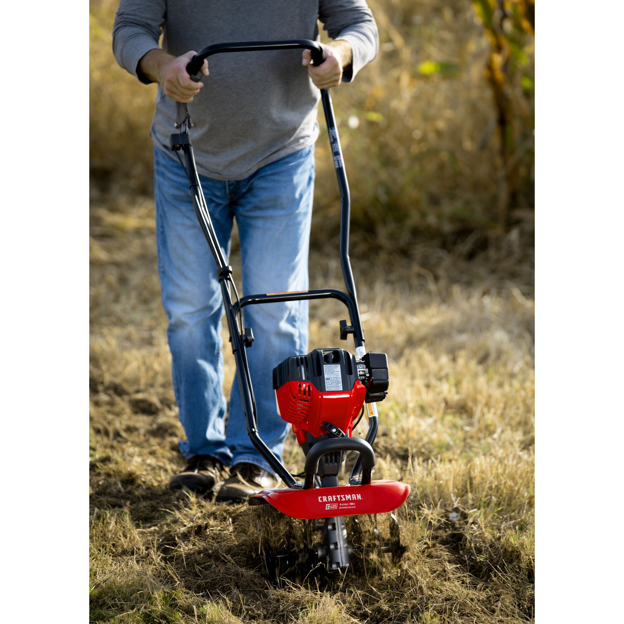 CRAFTSMAN gas cultivator in front view cultivating field in jeans and gray shirt