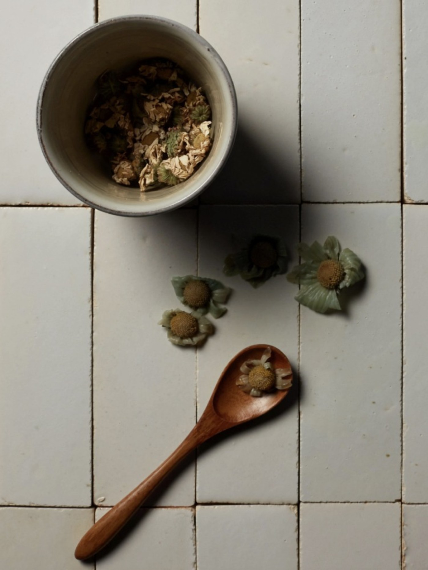 a bowl of flower buds and a wooden spoon on a tiled surface.