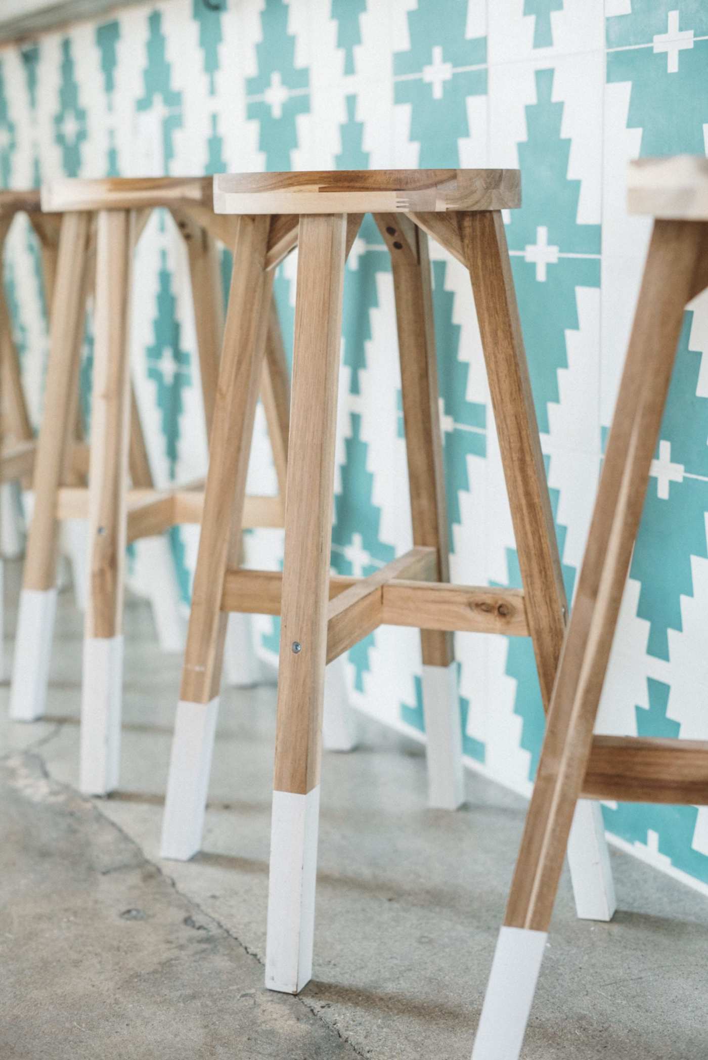 four wooden stools in front of a tiled counter.