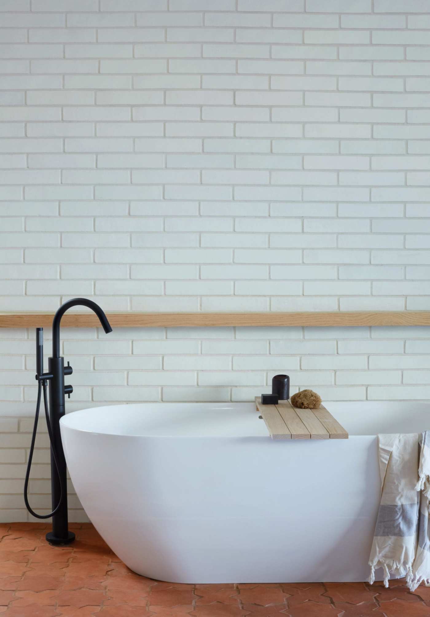 a white bathtub in a bathroom with a red terracotta floor and white tiled walls.