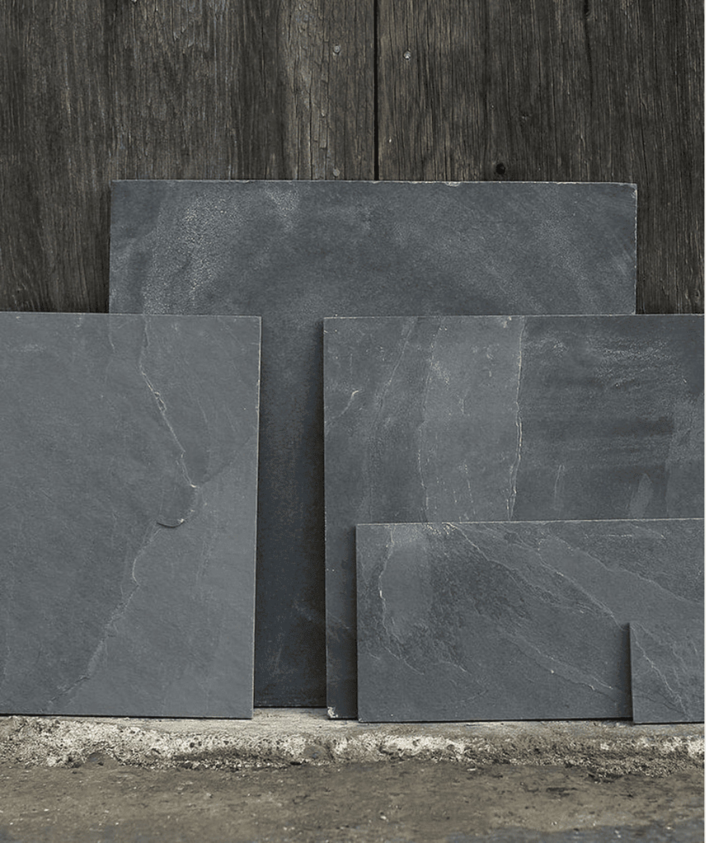 four various sizes of slate tiles leaning against a wooden surface.