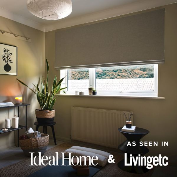 Grey fabric Roman blind, lowered about three-quarters with a neat hem, filtering soft daylight. Cozy neutral living room with tall snake plant, side tables, candle, radiator, tiled roof and distant treeline.
AS SEEN IN
Ideal Home &
Livingetc