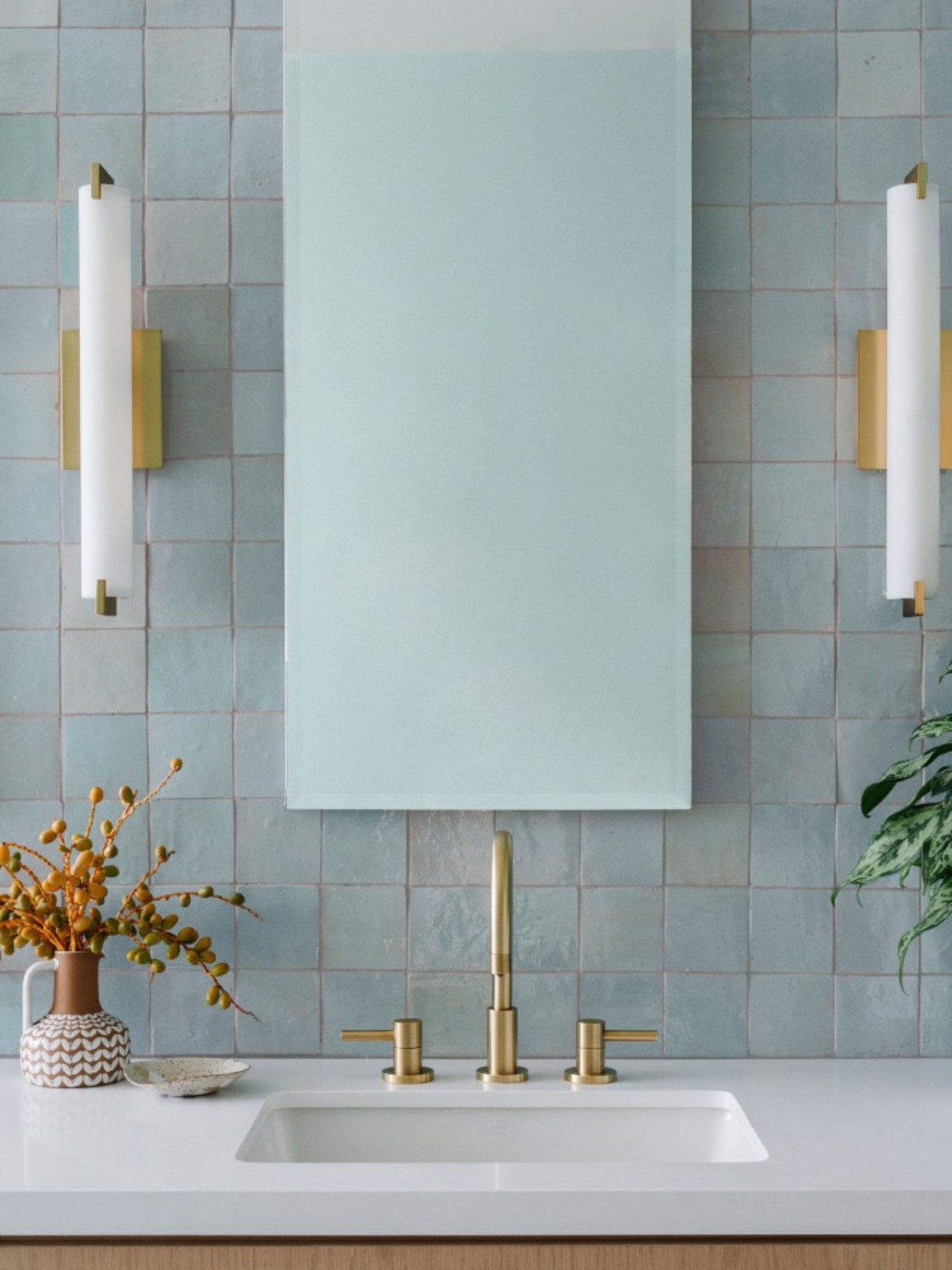 a bathroom with a mirror, a blue tiled wall and gold fixtures.